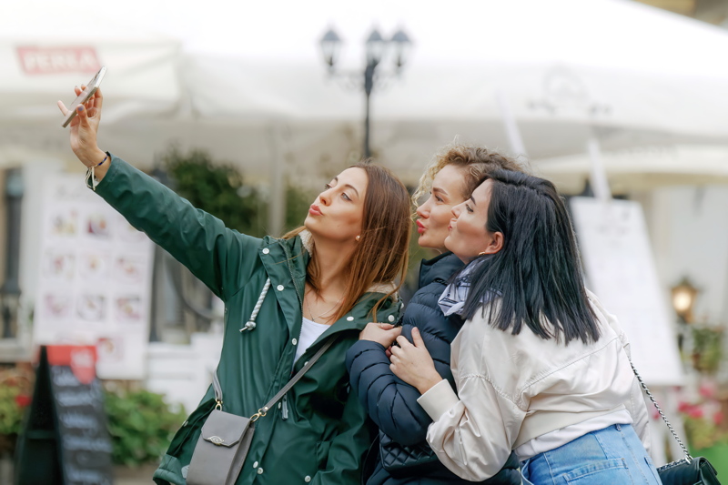 1 - Three individuals outdoors in casual clothing, featuring outerwear like a dark green hooded jacket and a small crossbody bag